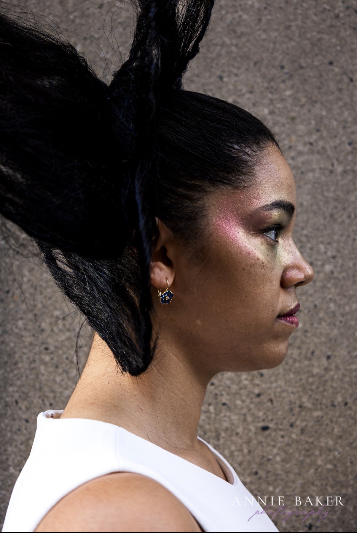 Side profile of a model with a sculptural high ponytail and shimmering editorial cheek color
