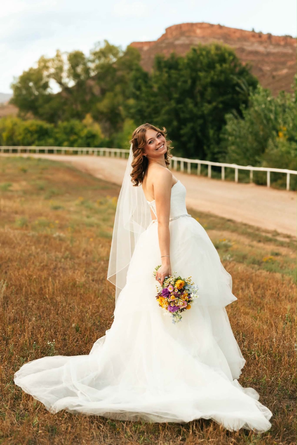 Bride with soft curls and veil holding a wildflower bouquet in Colorado red rocks